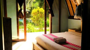 A bedroom with a wooden bed, a view of a garden, and a glass door leading outside. - Apit Lawang Villas (Penida Island)