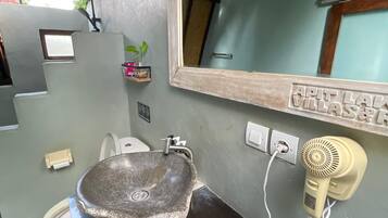 Un bagno con un lavabo in pietra, uno specchio, un asciugacapelli e un piccolo ripiano con una pianta.