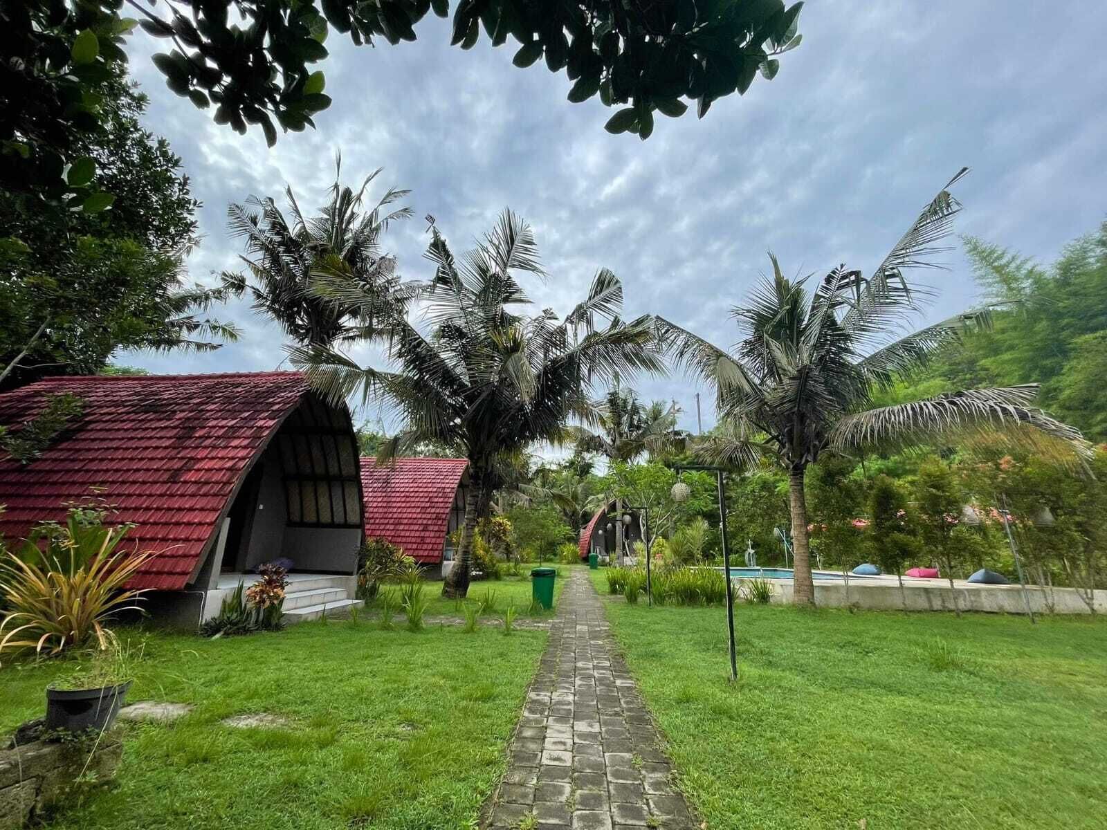 A pathway leading to a building with a red roof, surrounded by lush greenery and palm trees.