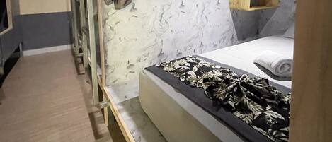 A compact bedroom with a bunk bed, a small bedside table, a hanging light, and a marble-patterned wall.