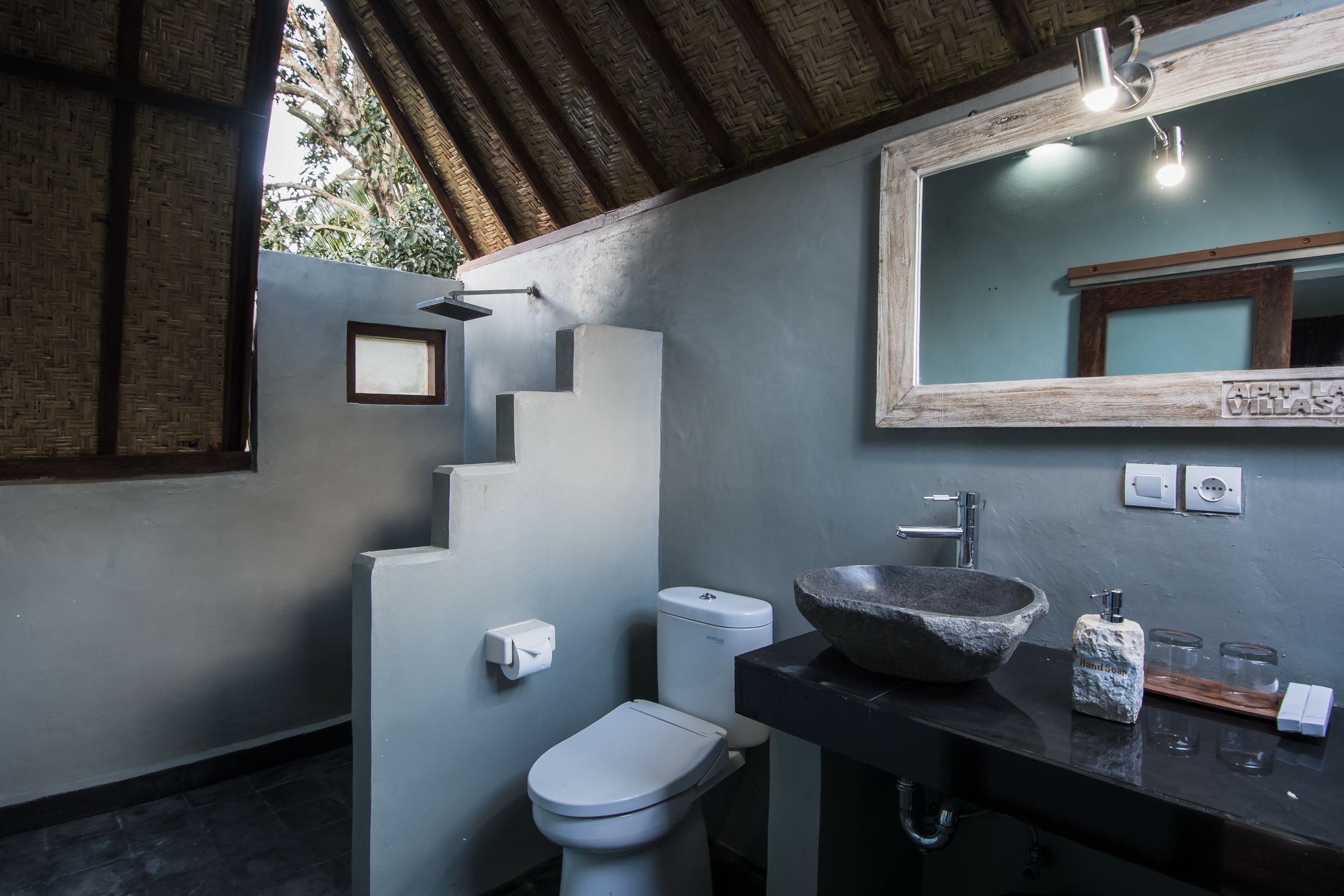 A modern bathroom with a stone sink, a white toilet, and a mirror with a wooden frame.