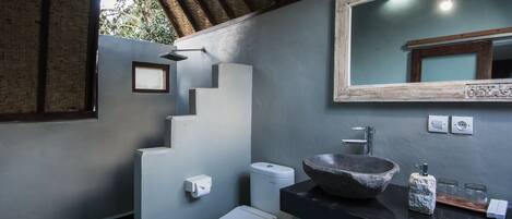 A modern bathroom with a stone sink, a white toilet, and a mirror with a wooden frame.