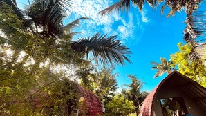 A tropical garden with a thatched-roof structure, lush greenery, and a clear blue sky. - Apit Lawang Villas (Penida Island)