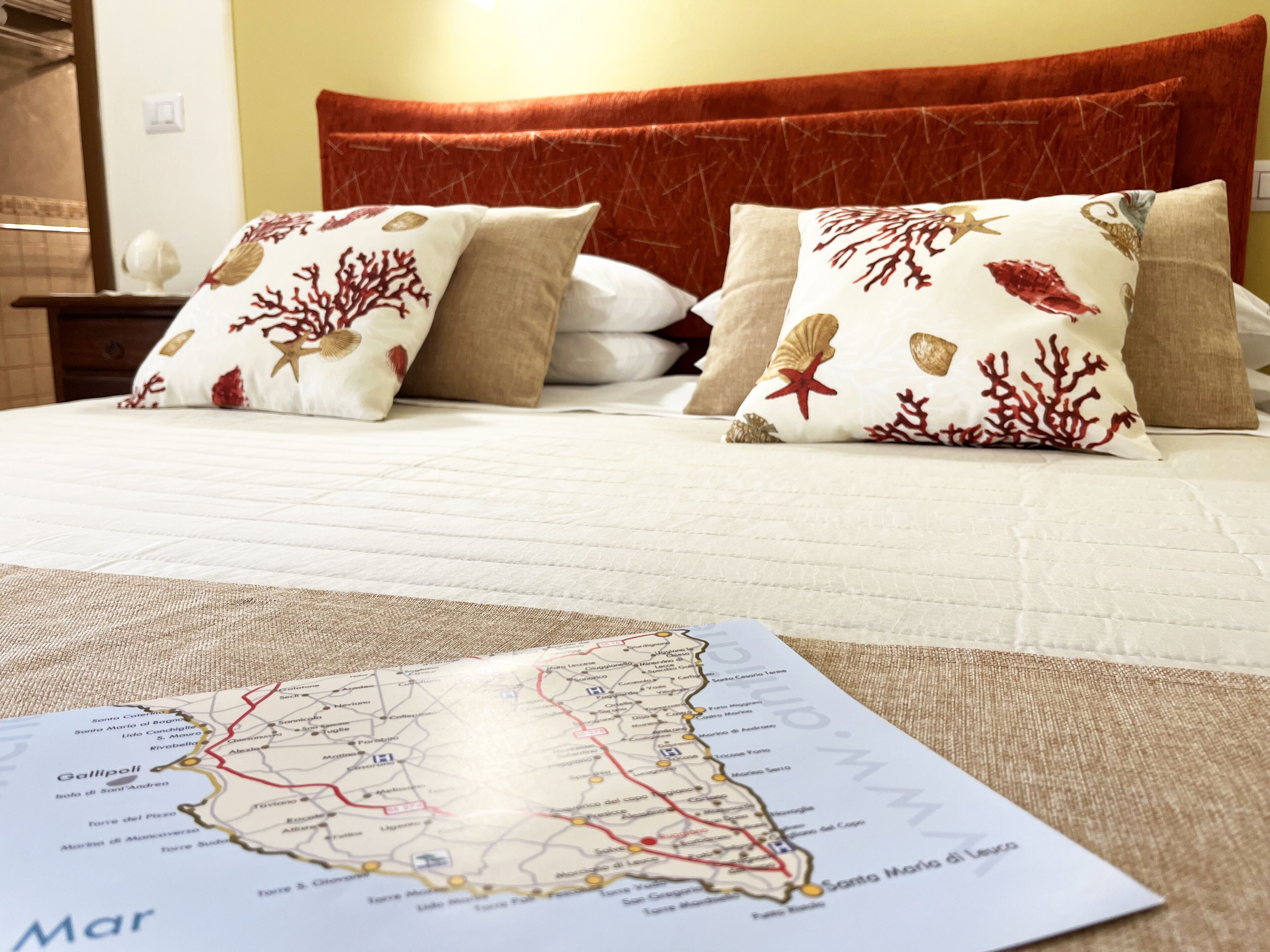 A bed with a red headboard, white bedding, and decorative pillows with marine designs. A map of a coastal region is visible on the bed.