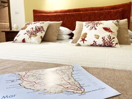 A bed with a red headboard, white bedding, and decorative pillows with marine designs. A map of a coastal region is visible on the bed.