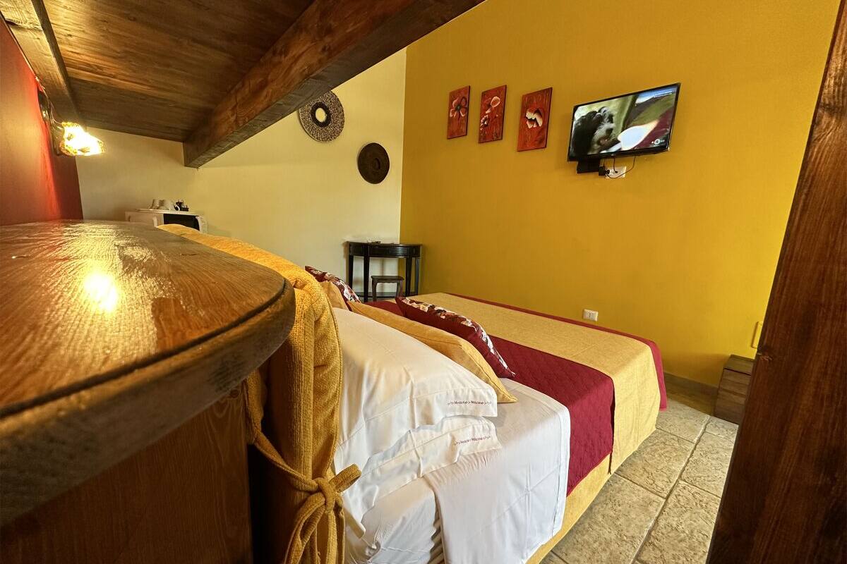 Une chambre d’hôtel avec un plafond en bois, un lit avec une literie blanche et rouge, un téléviseur fixé au mur et une petite table avec une chaise.
