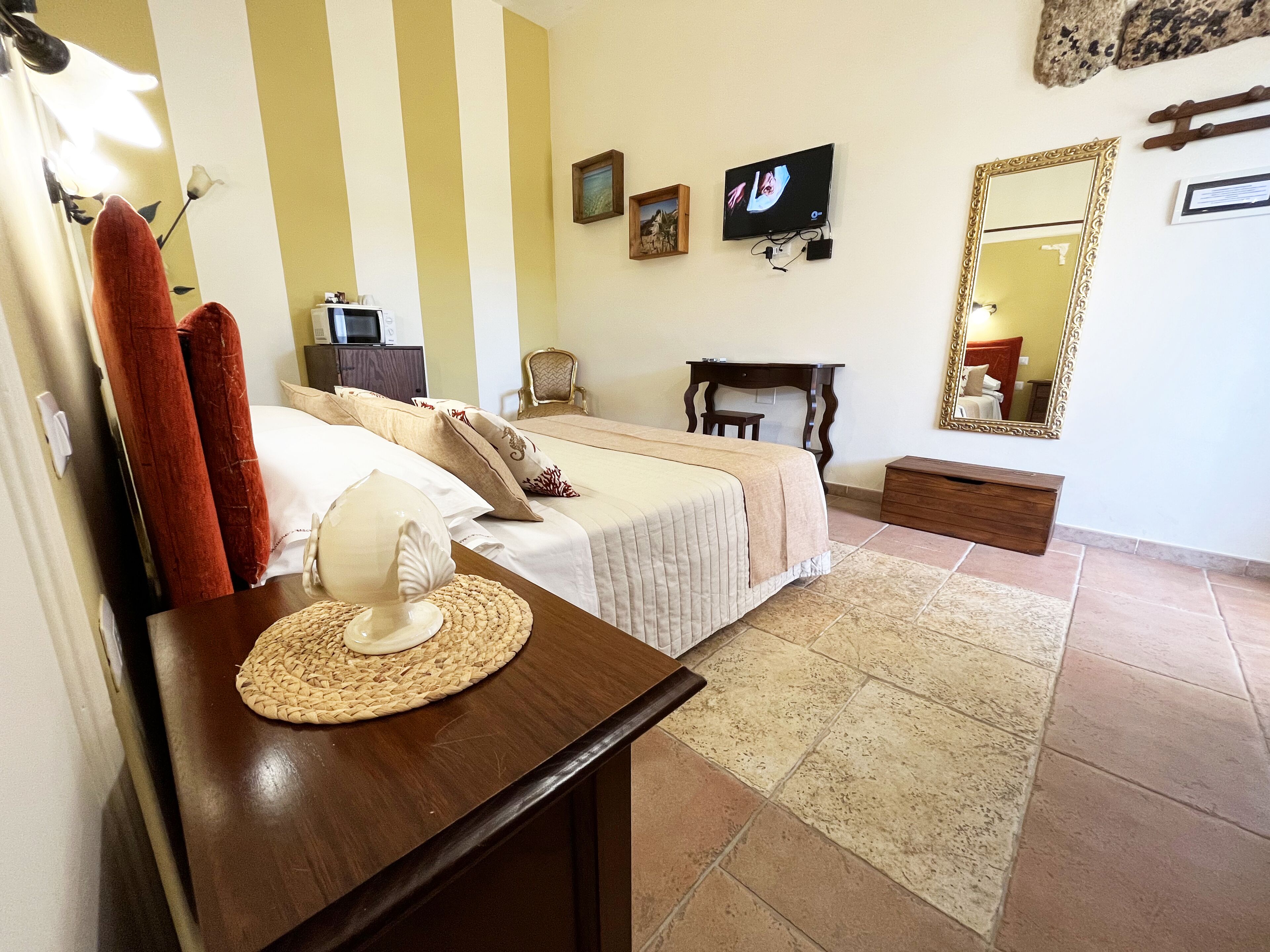 Una habitación de hotel con cama, mesita de noche, televisor, cómoda y un espejo grande.