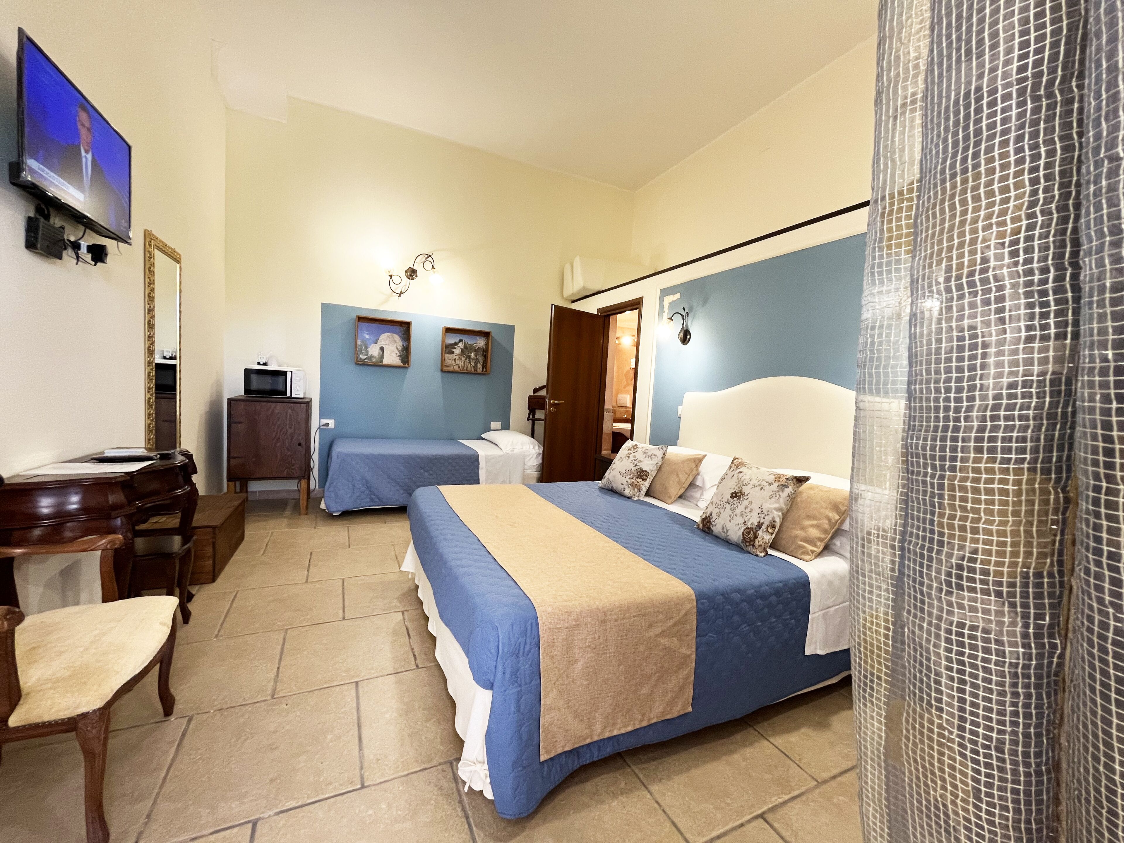 Hotelkamer met twee bedden, een bureau, een stoel, een televisie en een zichtbare badkamer door een geopende deur.