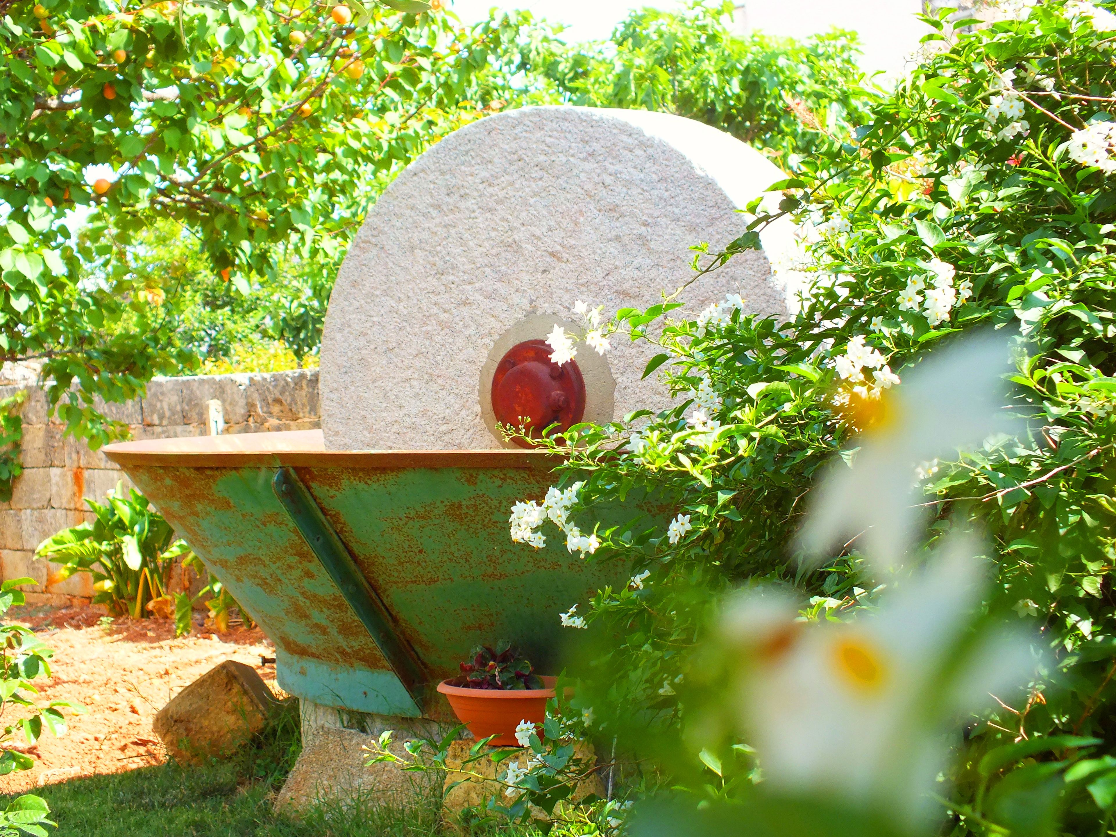 A stone oven with a red interior, surrounded by greenery and a rusty metal structure.
