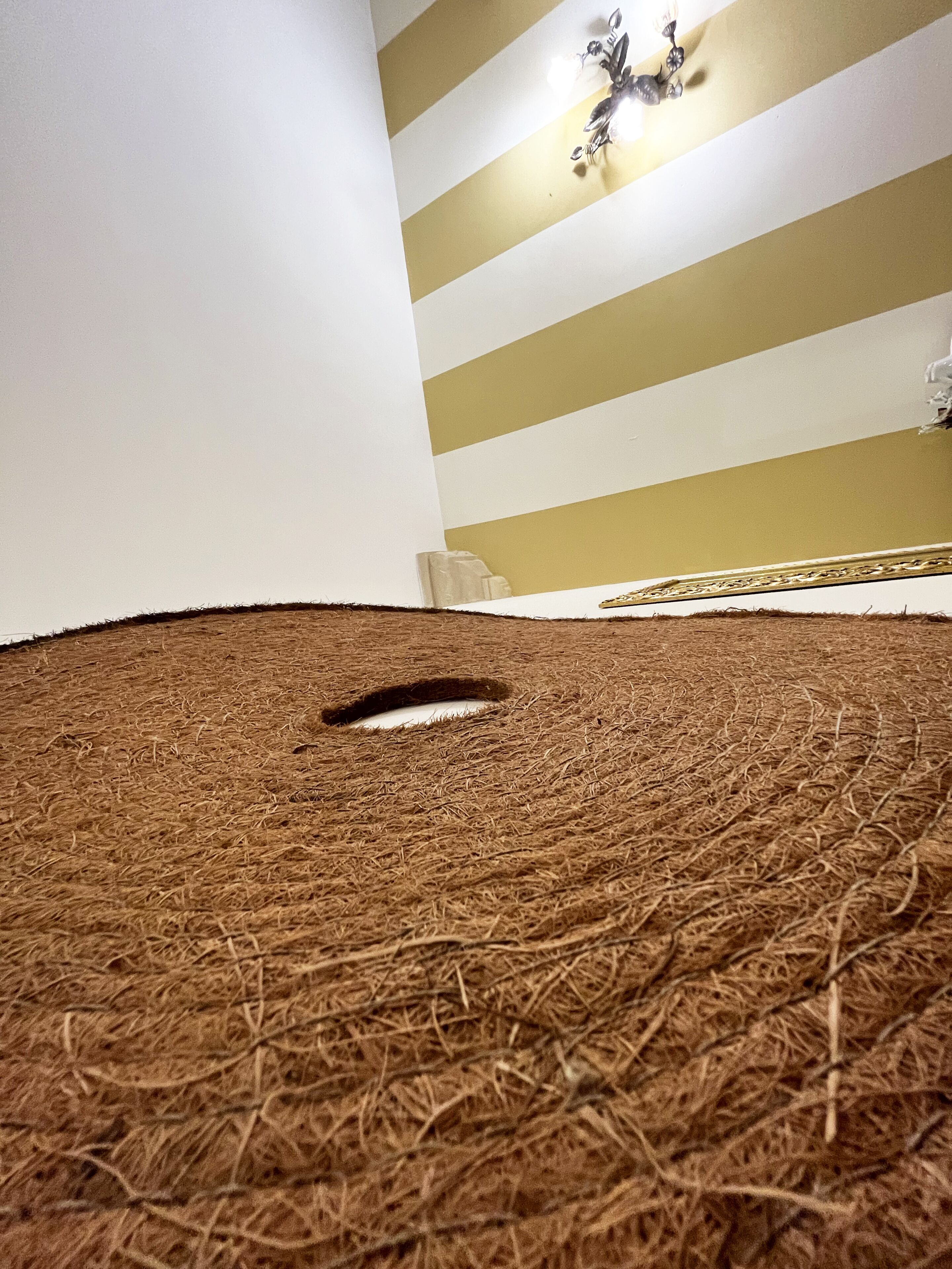 A room with a straw carpet, a white wall, and a striped wall with a chandelier.