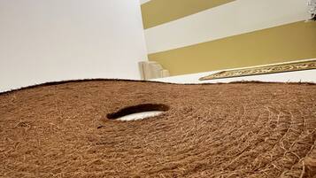 A room with a straw carpet, a white wall, and a striped wall with a chandelier.