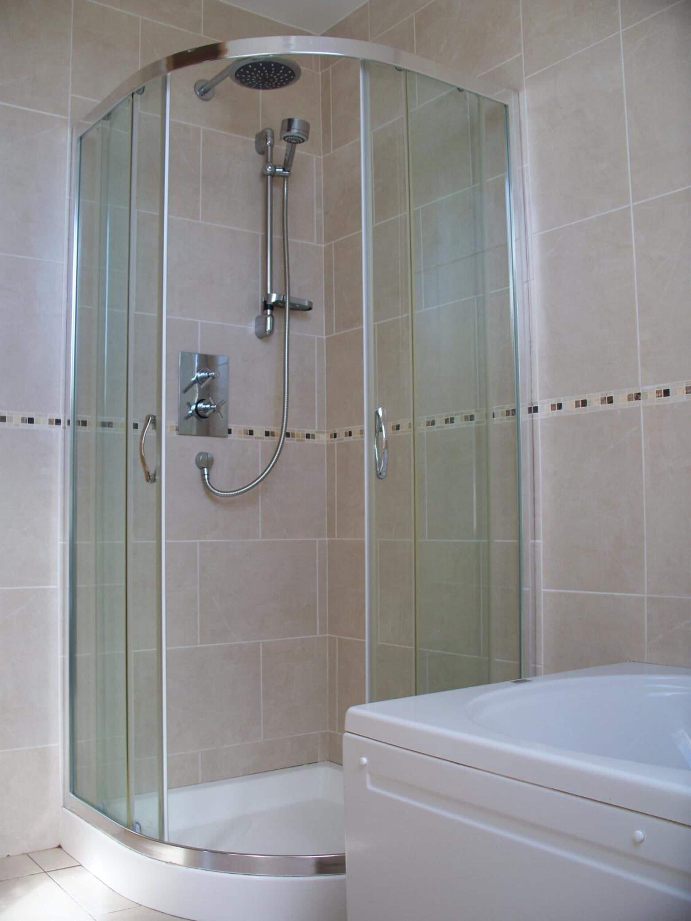 A glass-enclosed shower with a handheld showerhead and a wall-mounted faucet.