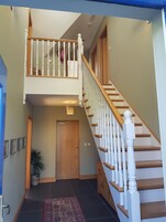 Una escalera con balaustres blancos y peldaños de madera que conduce a un nivel superior. Se observa una puerta de madera al pie de la escalera.