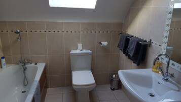 Un baño con tragaluz, bañera, inodoro y lavamanos.