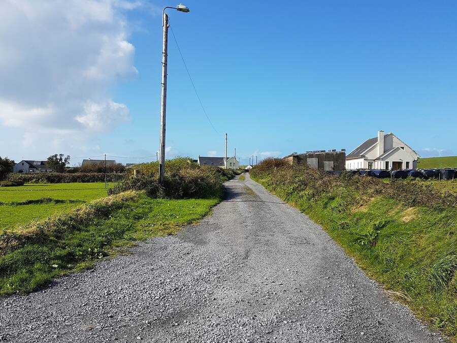 A rural road leading to houses with a clear sky.