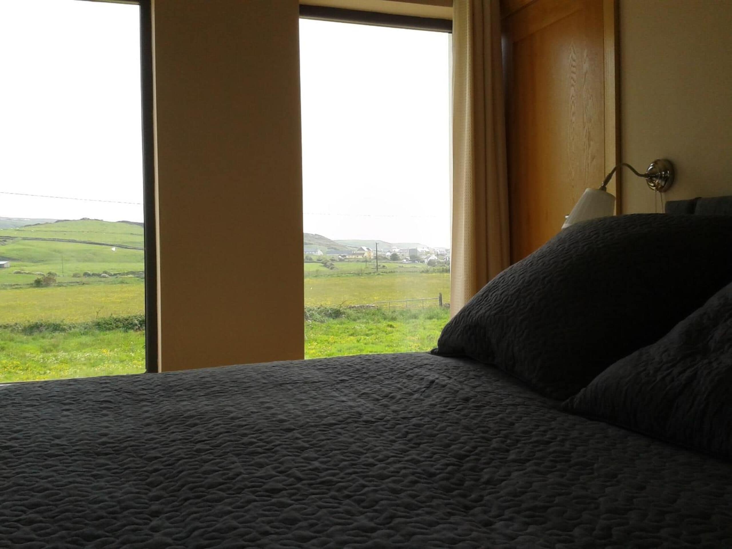 A bedroom with a large window offering a view of a green landscape.