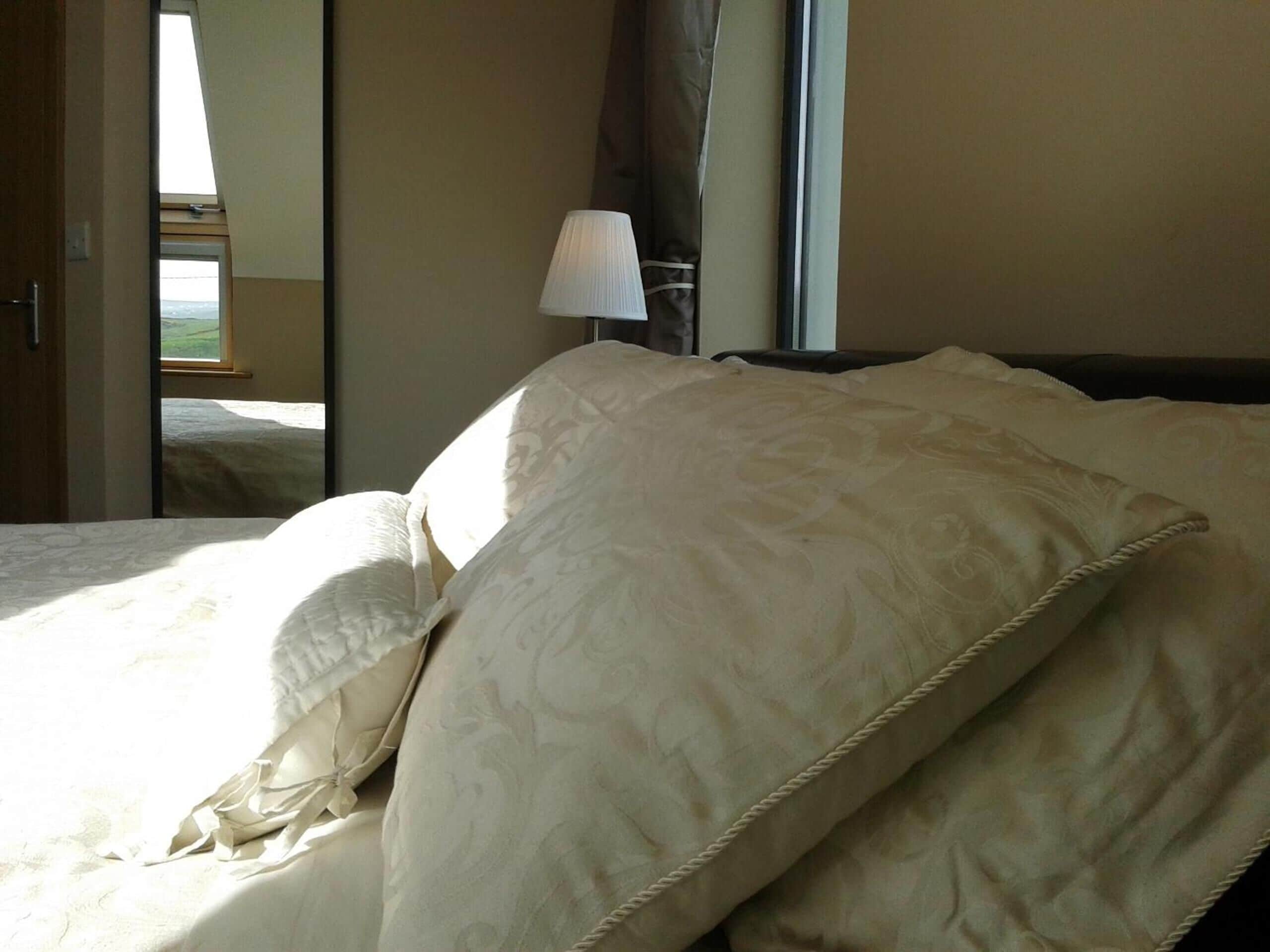 A hotel room with a bed, a lamp, and a view of the outdoors through a window.