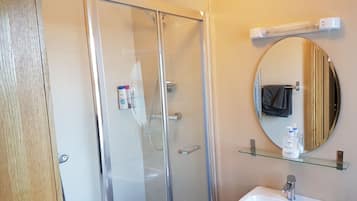 Een moderne badkamer met een douchecabine van glas, een witte wastafel, een ronde spiegel en toiletartikelen op een glazen plank.
