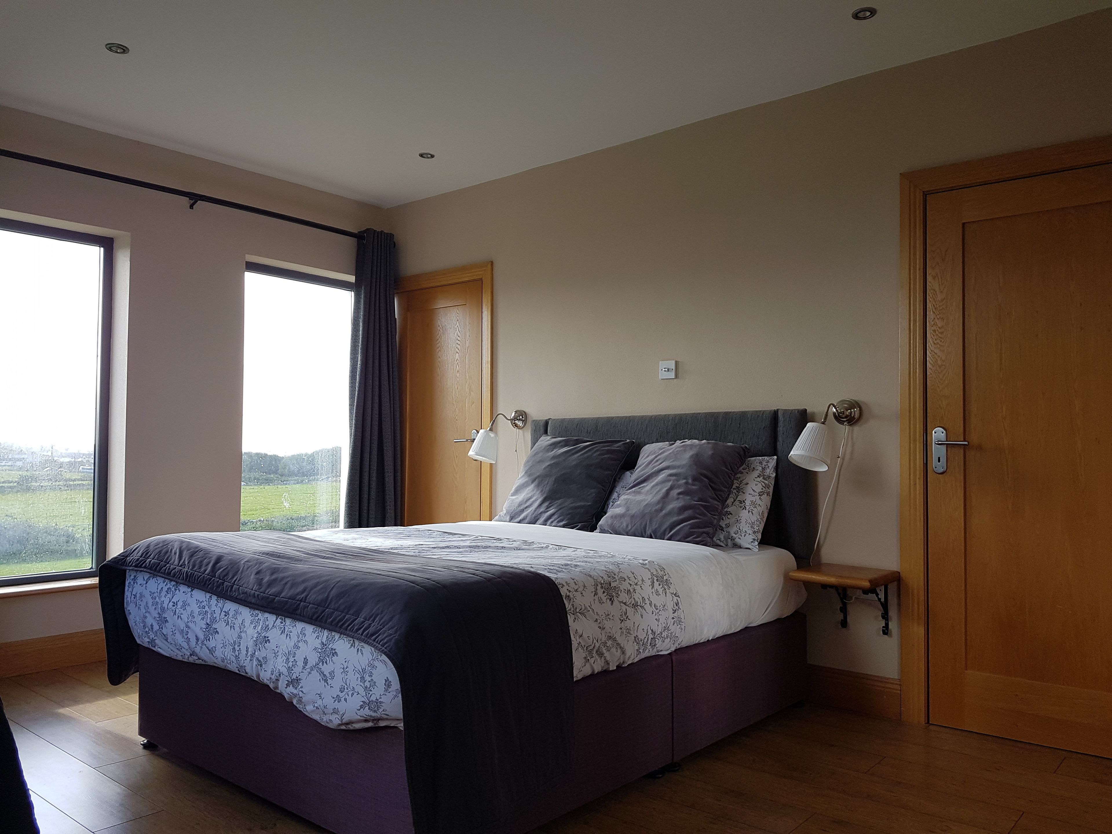 Une chambre à coucher avec un lit, des lampes de chevet, une table de nuit et une vue sur l’extérieur.