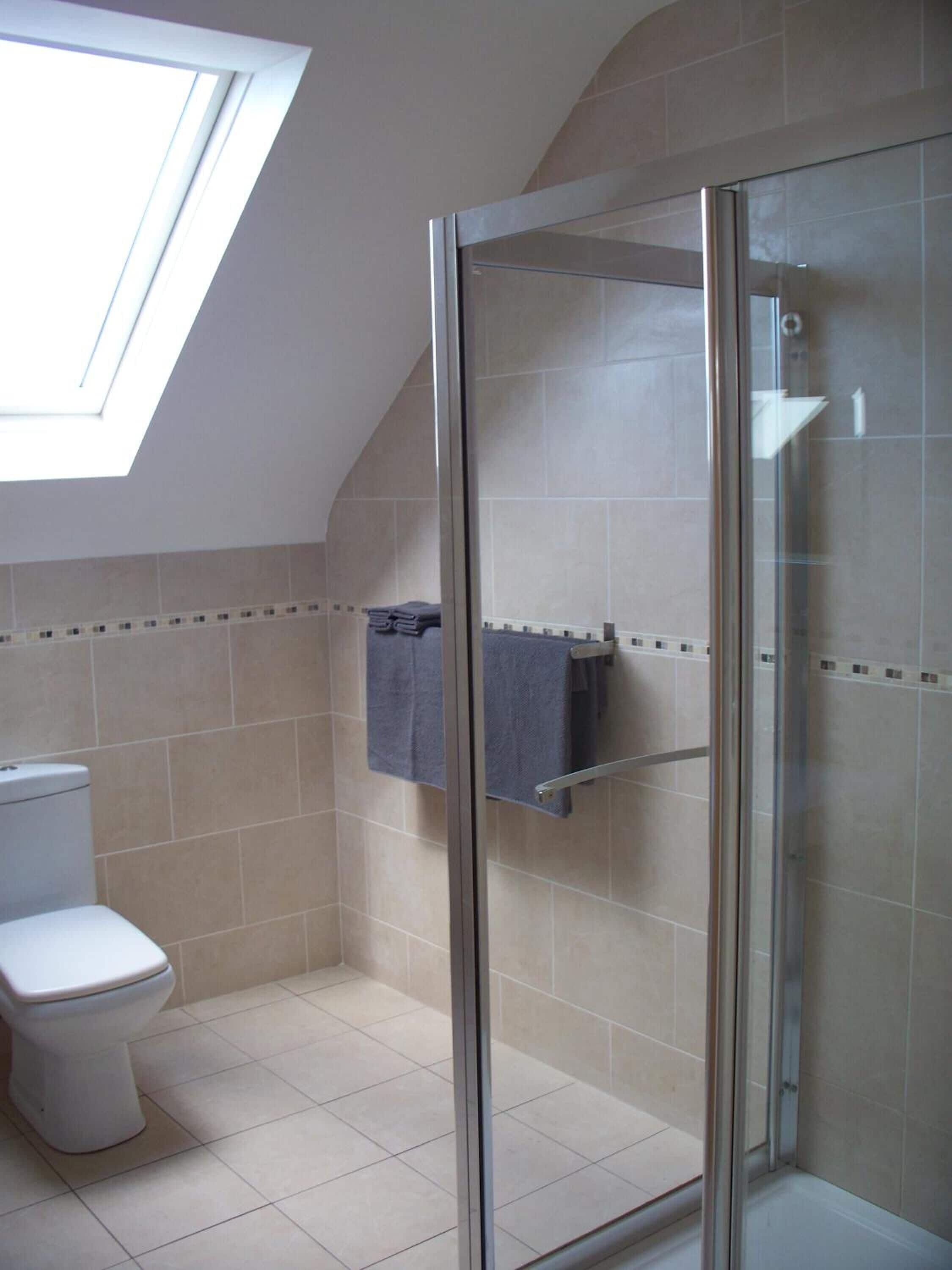 A bathroom with a glass shower enclosure, a toilet, and a towel rack.