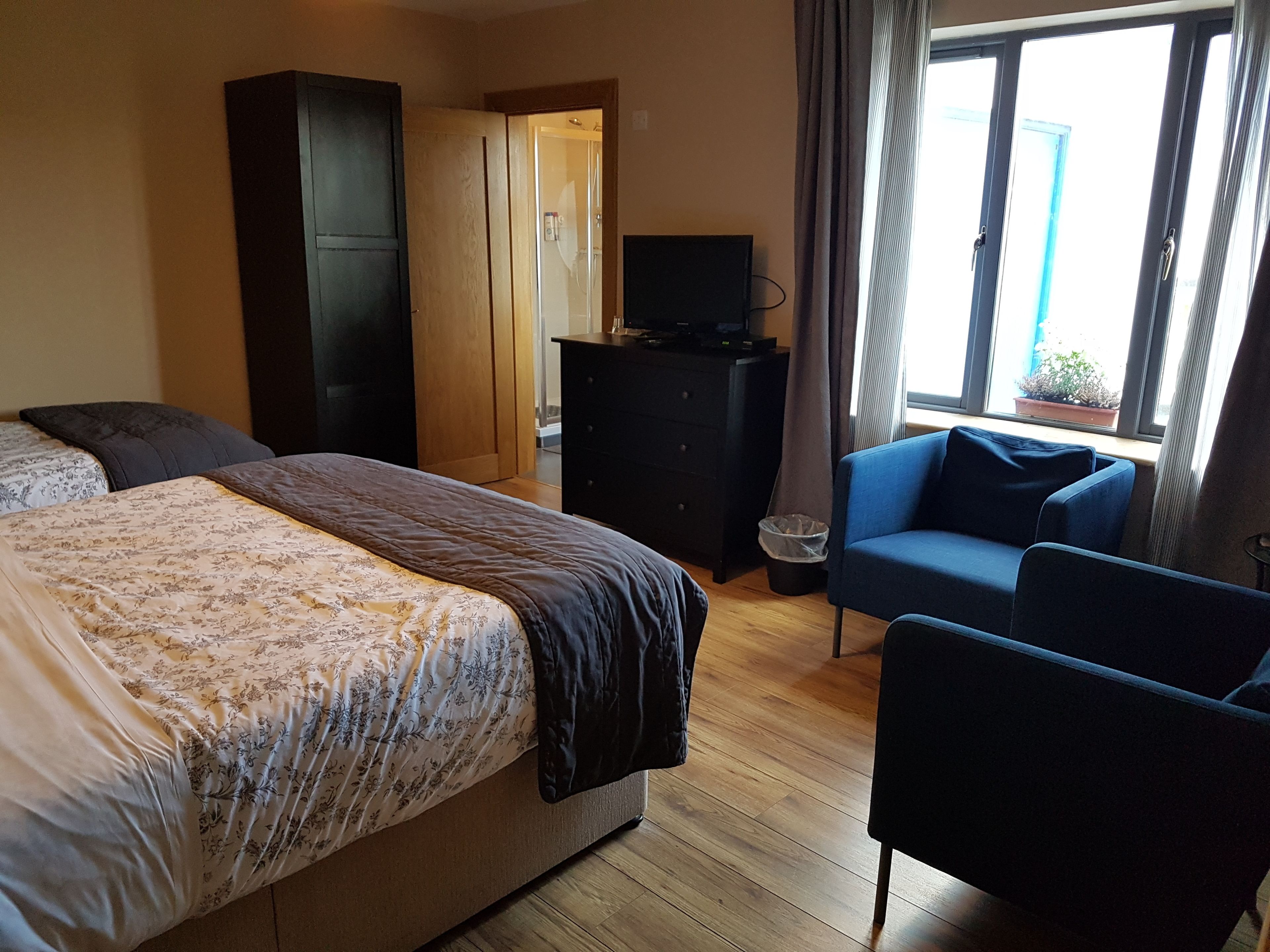 Une chambre à coucher comprenant un lit, une commode, un téléviseur, une chaise et une fenêtre donnant sur l’extérieur.