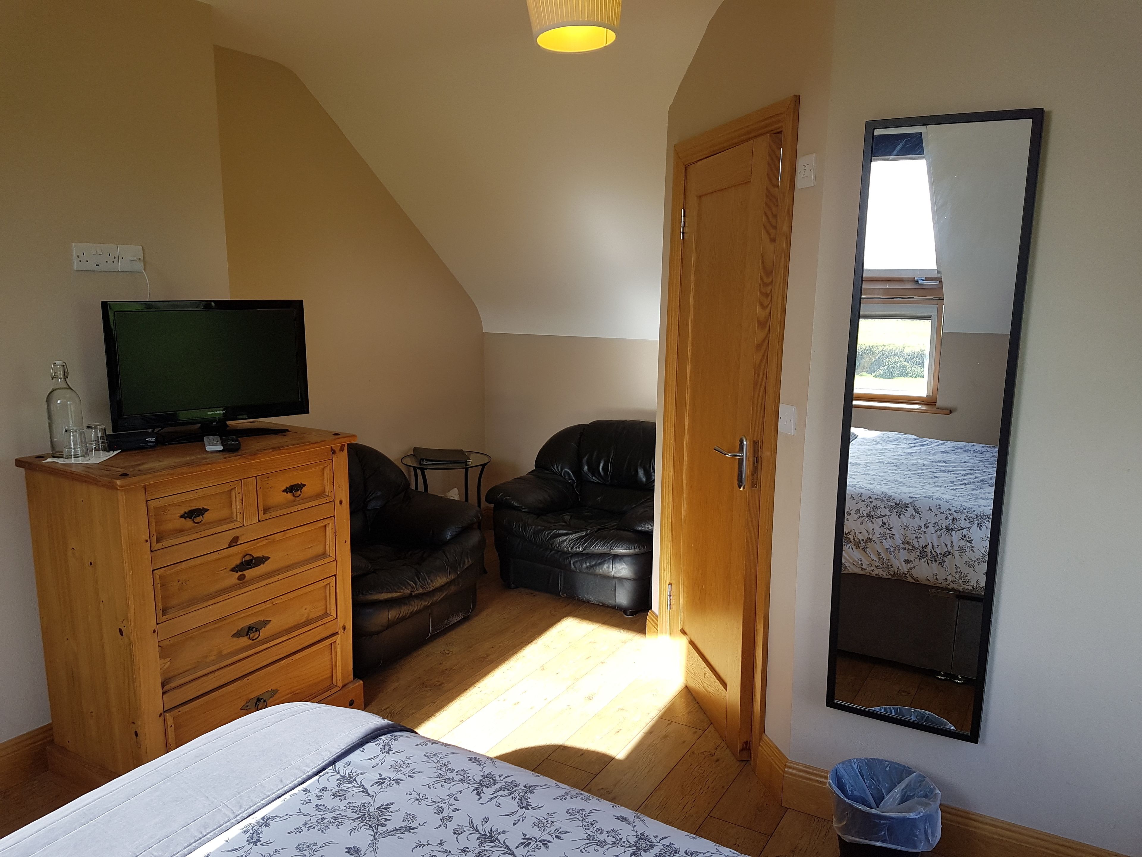 A bedroom with a bed, wooden dresser, television, leather chair, and a large mirror.