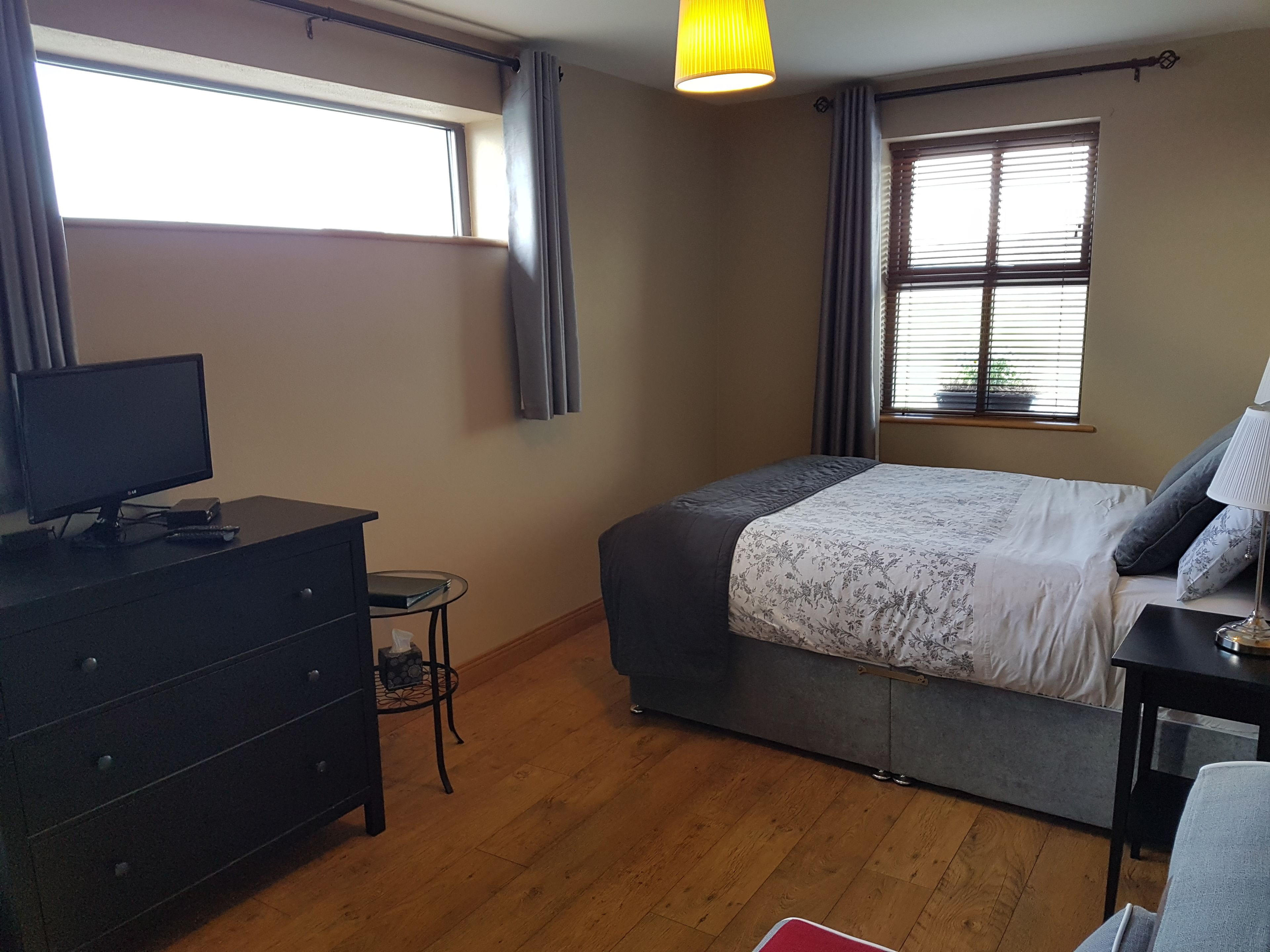 A bedroom with a bed, a TV on a dresser, a lamp, and a window with curtains.