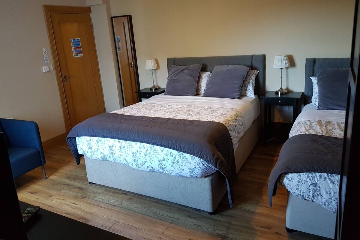 A hotel room with a large bed, two bedside tables, a chair, and a wooden floor.