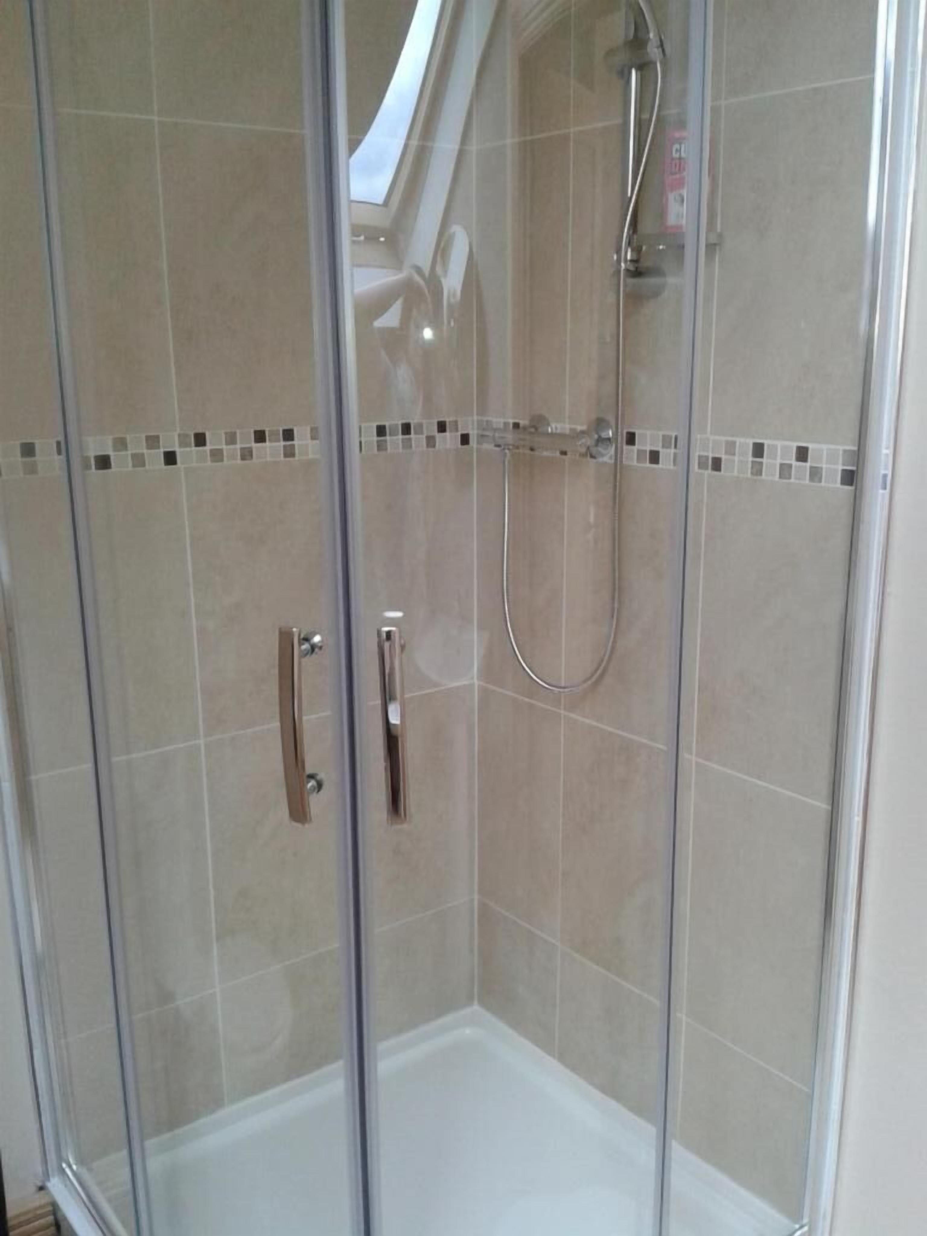 A glass-enclosed shower with a handheld showerhead and a wall-mounted faucet.