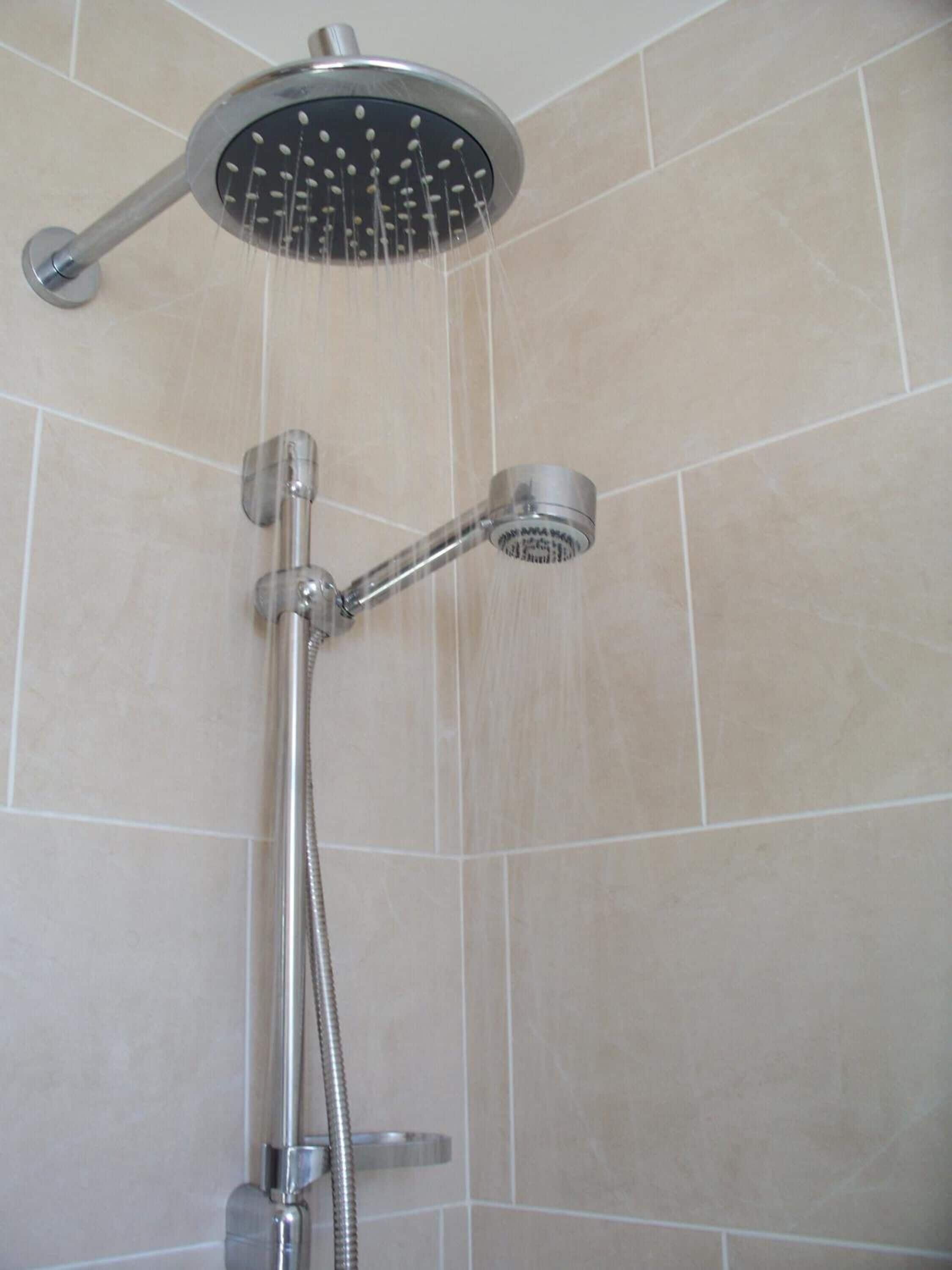 Une douche équipée d’un pommeau de douche à main et d’un pommeau de douche fixe au plafond.