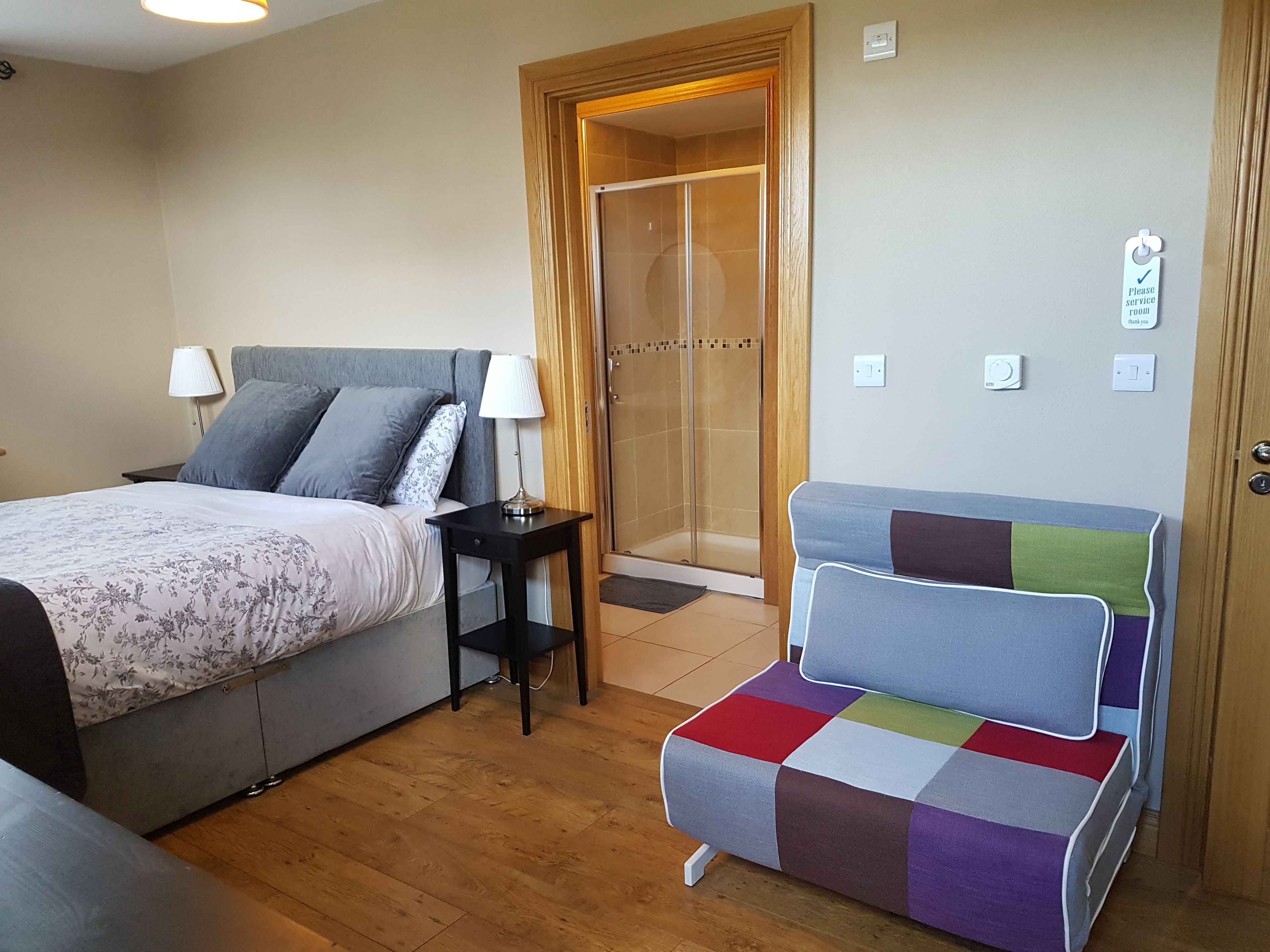 A bedroom with a bed, bedside table, lamp, and a colorful chair.