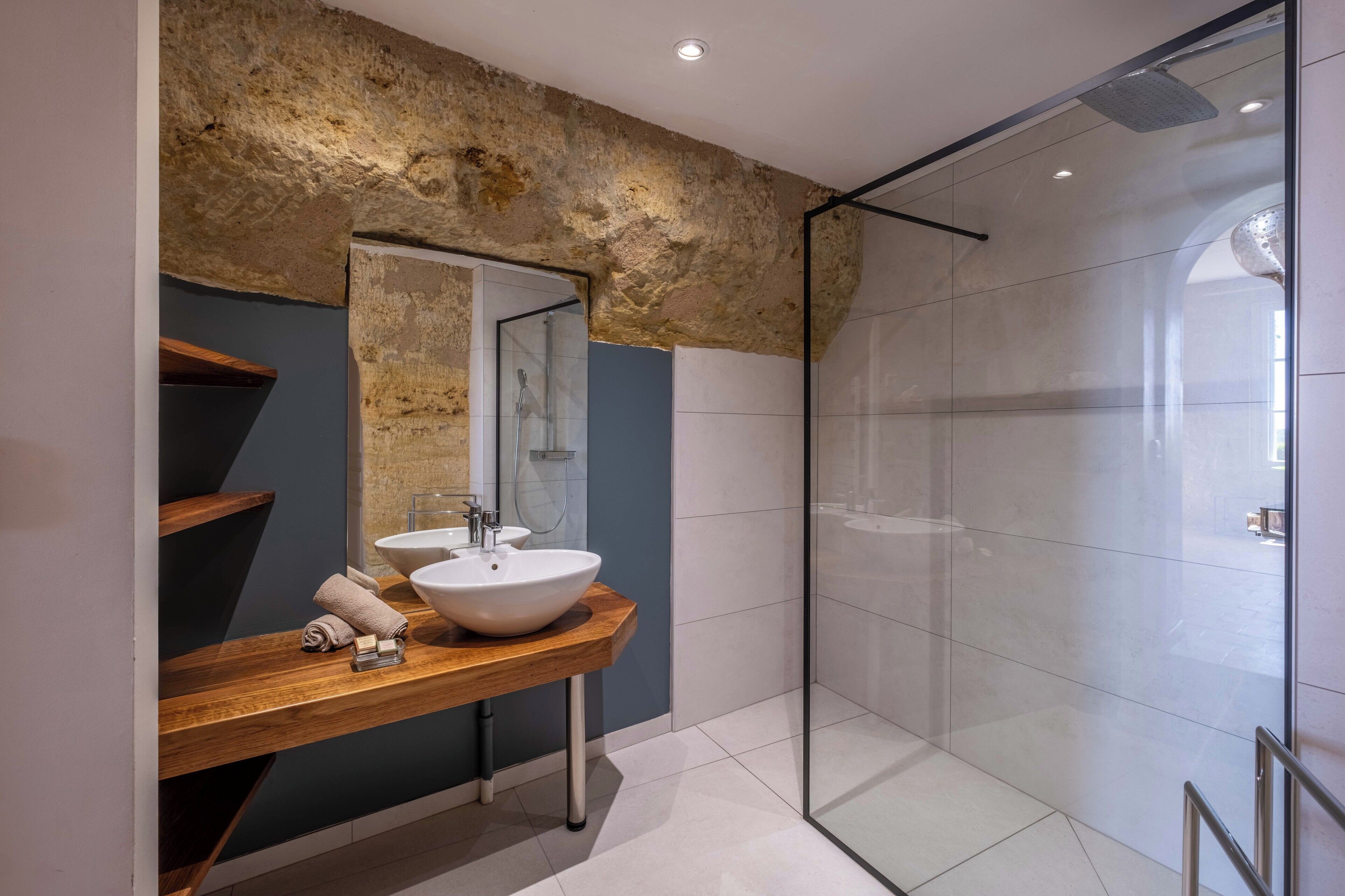 A modern bathroom with a stone accent wall, a wooden vanity, a white sink, and a glass shower enclosure.