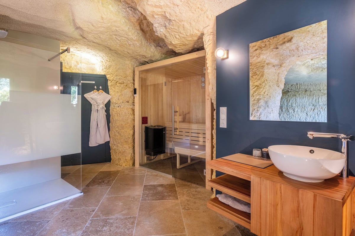 Une salle de bain moderne avec un mur en pierre, un meuble-lavabo en bois, un grand lavabo et une douche à parois de verre.