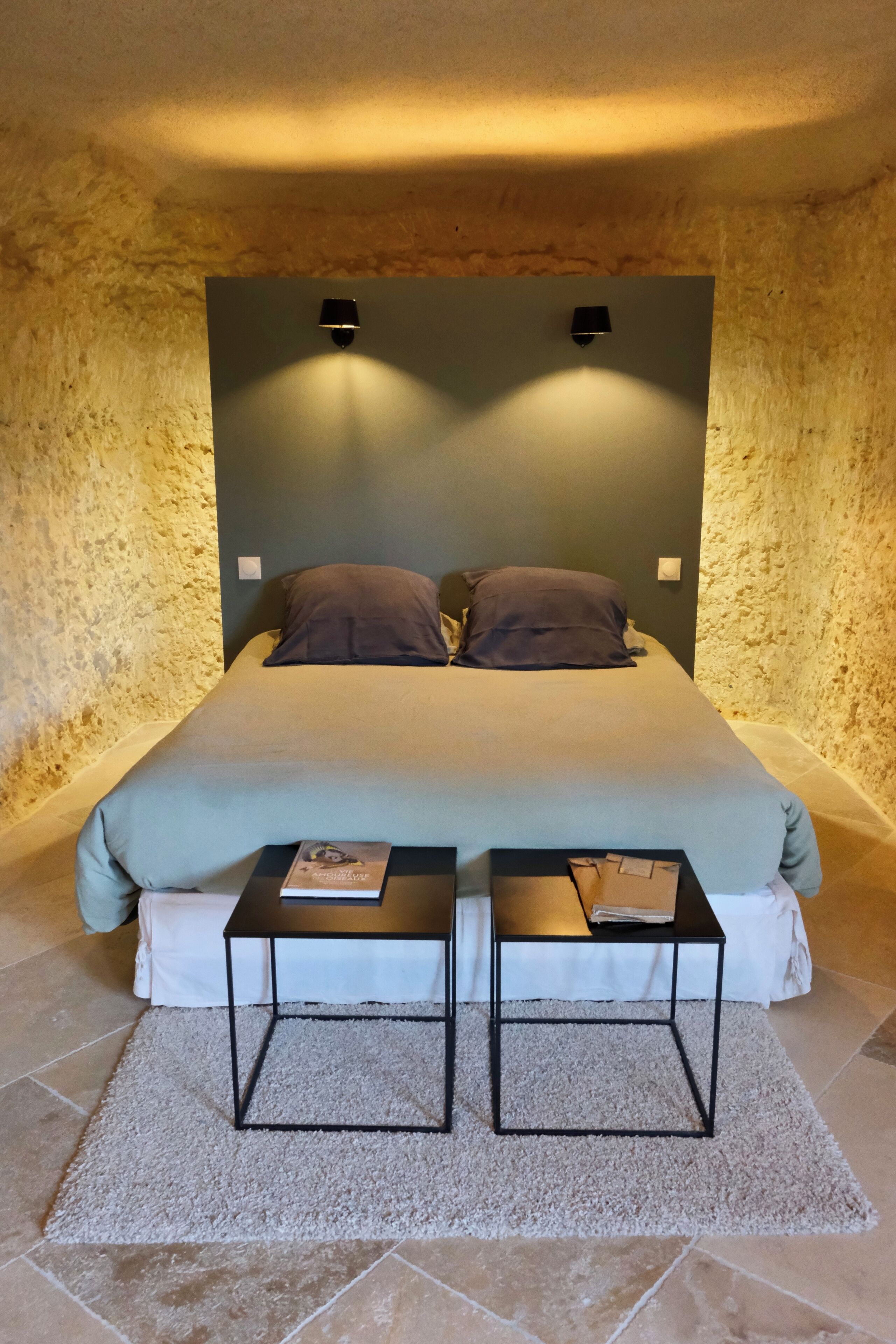 Un dormitorio con una cama grande, dos mesitas de noche y una pared de piedra con textura.