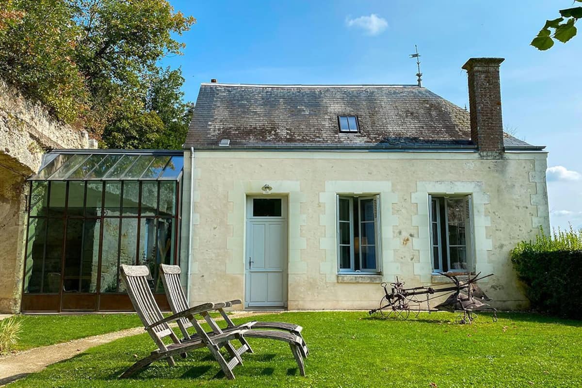 Une maison à deux étages avec une véranda en verre, une porte blanche et une cheminée.