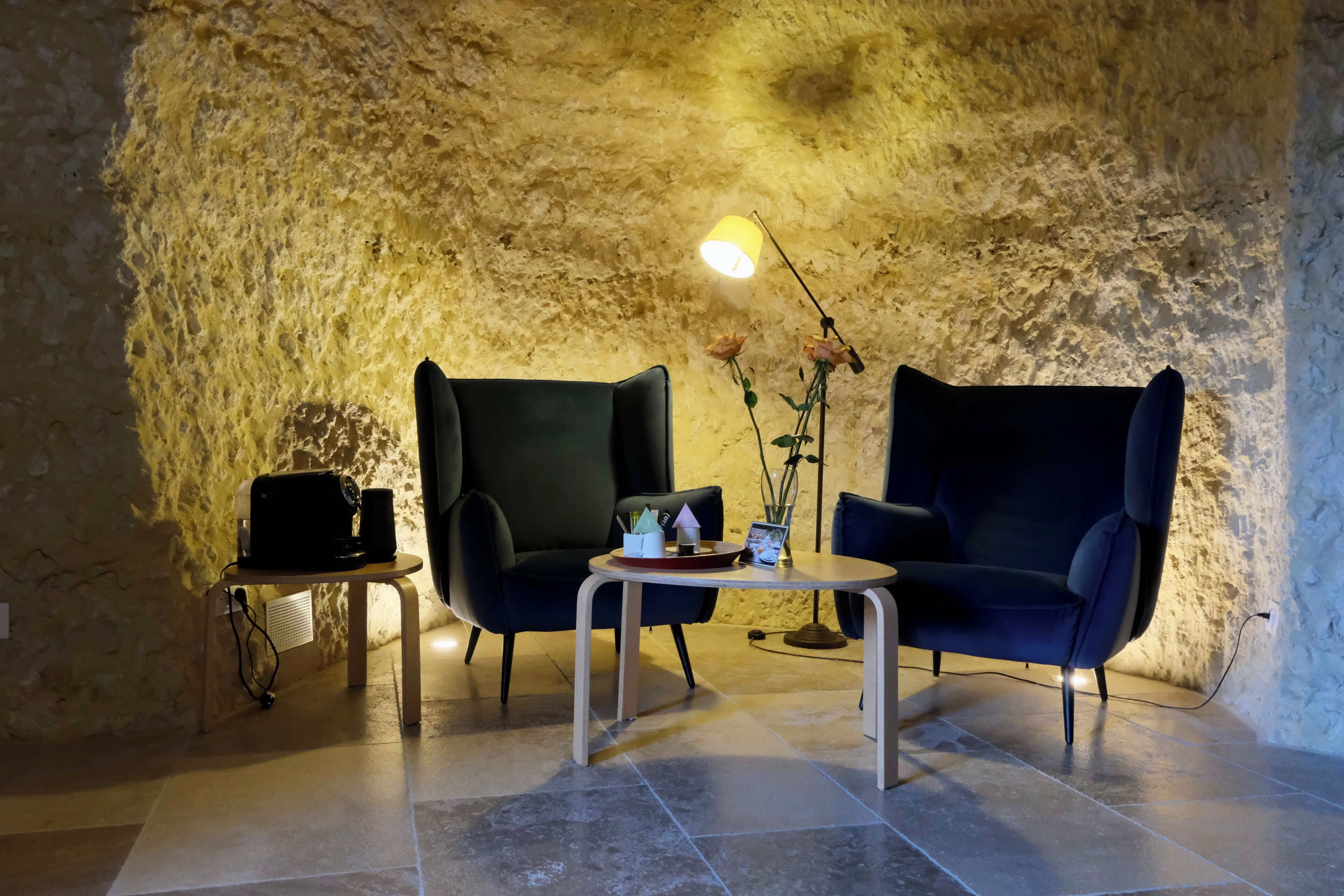A room with two dark chairs, a small table with a lamp, and a wall with a textured surface.