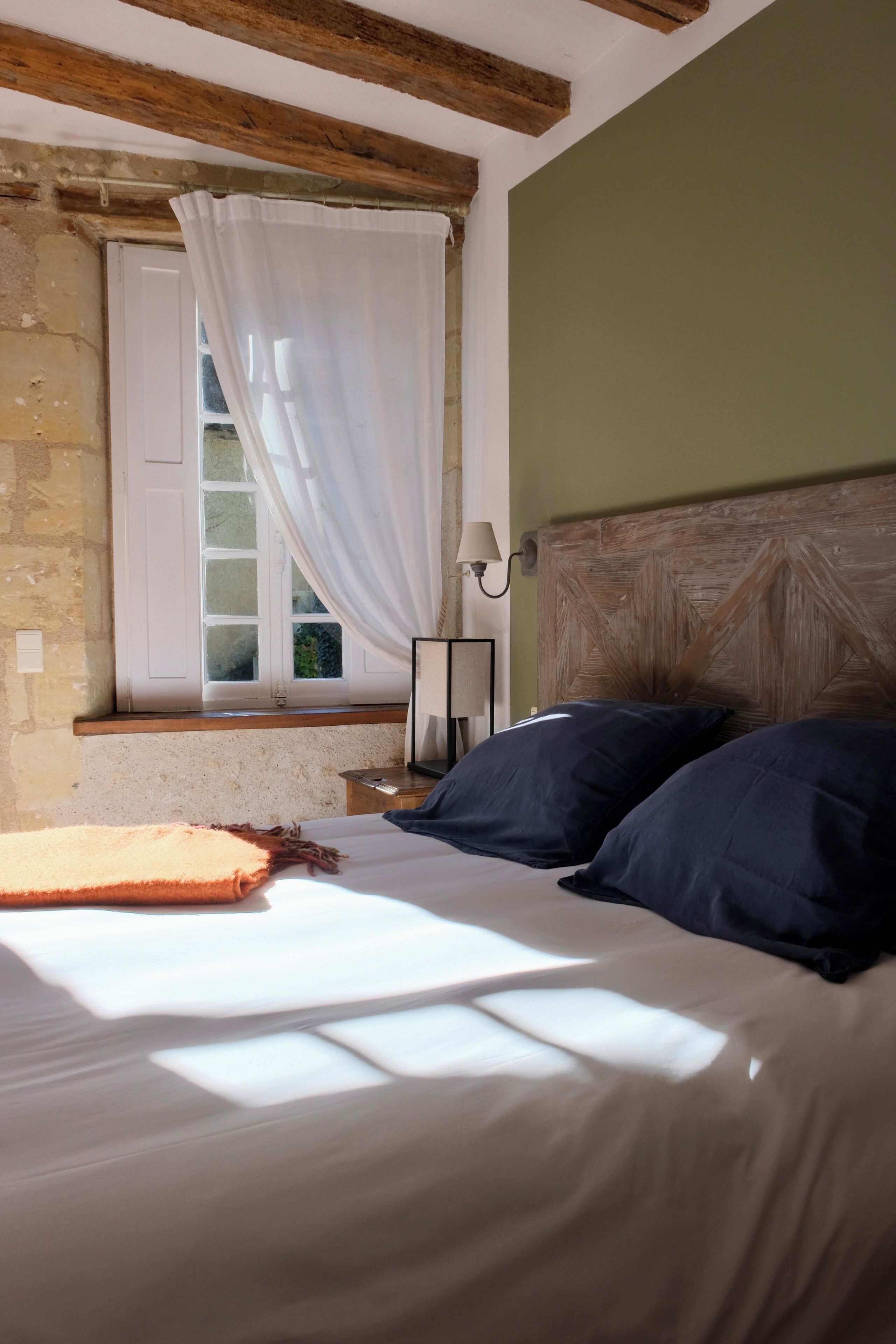 A bedroom with a bed, a window with curtains, a nightstand, and a lamp.