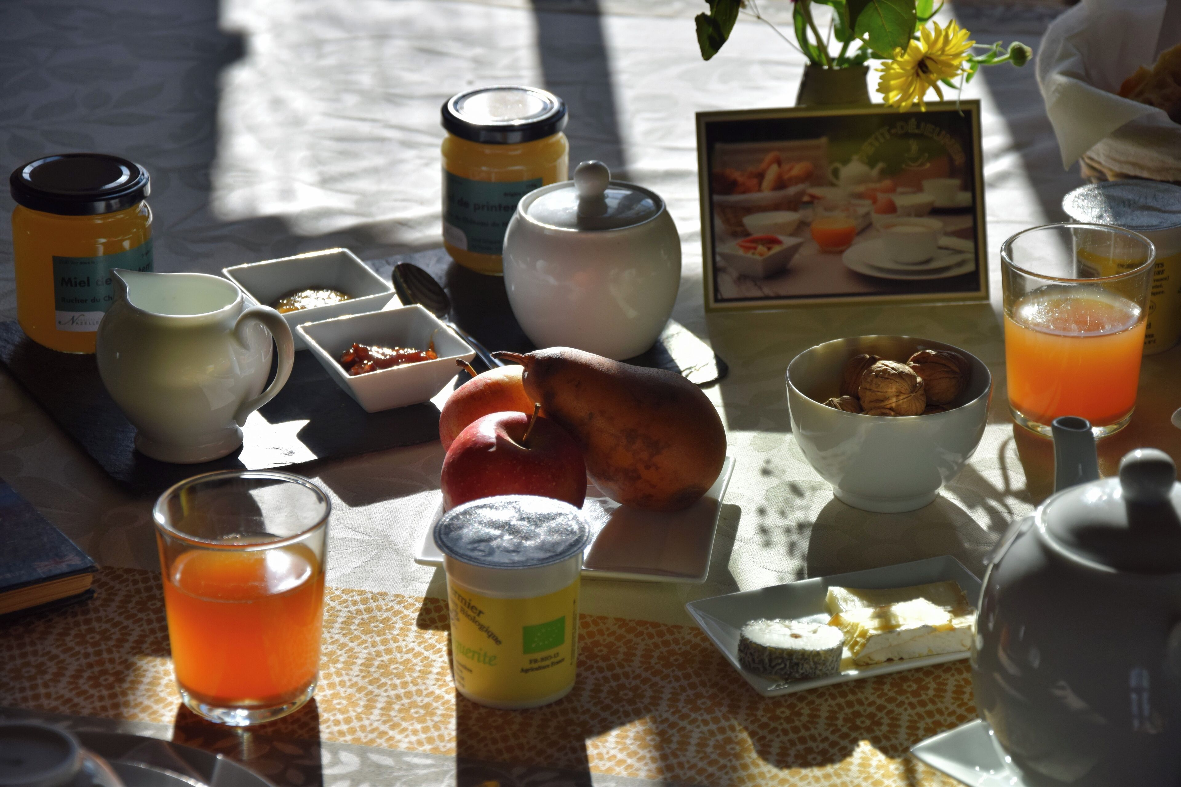 A breakfast table with various food items, a teapot, and a glass of orange juice.