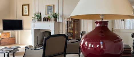 A living room with a fireplace, wooden beams, a large red lamp, and a television.