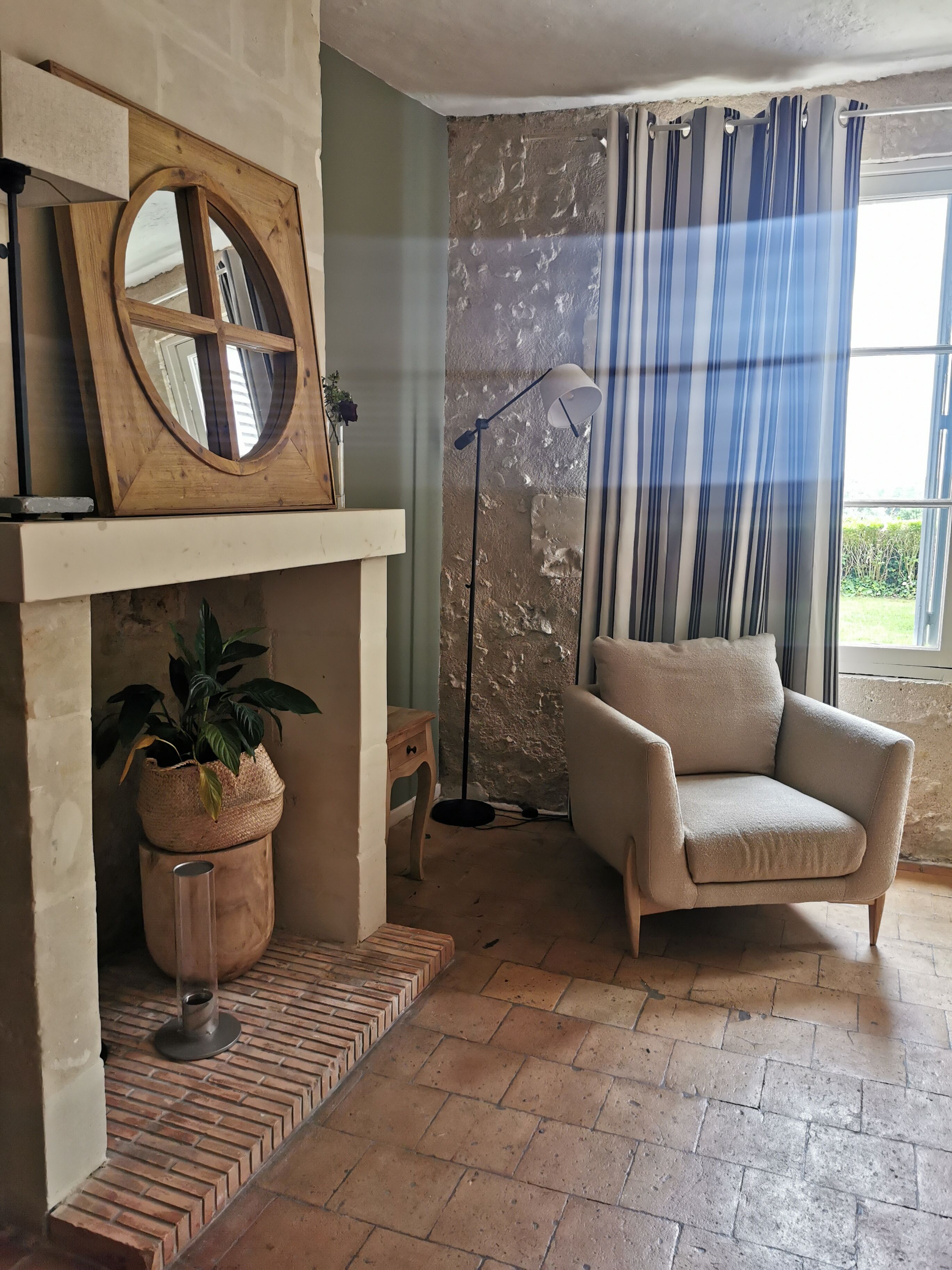 A living room with a fireplace, a potted plant, a floor lamp, and a beige armchair.