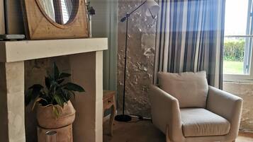 A living room with a fireplace, a potted plant, a floor lamp, and a beige armchair.