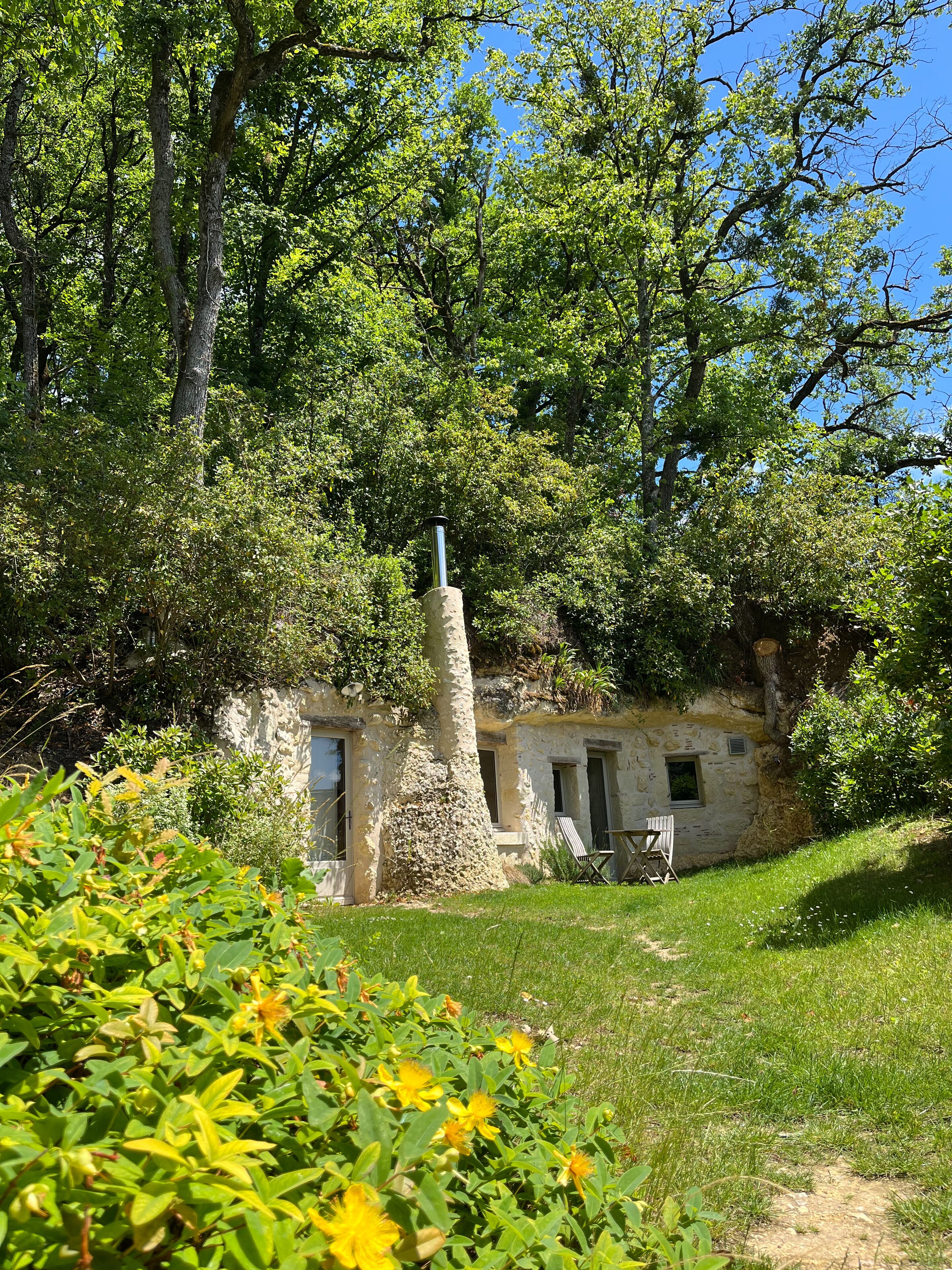 A rustic stone building with a chimney, surrounded by lush greenery and trees.