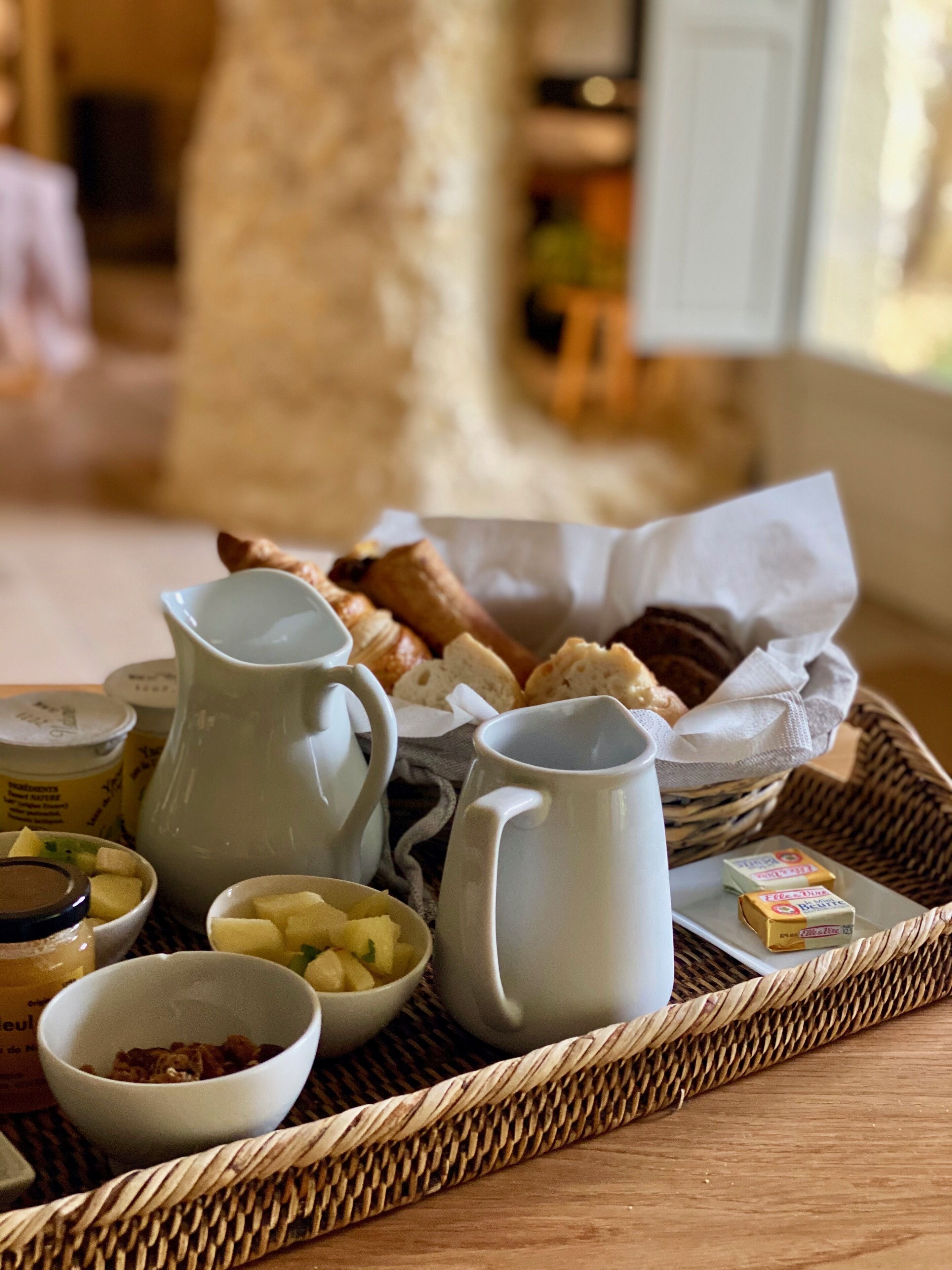 Ein Frühstücksbrett mit Brot, Butter, Marmelade und einer Karaffe auf einer gewebten Matte.