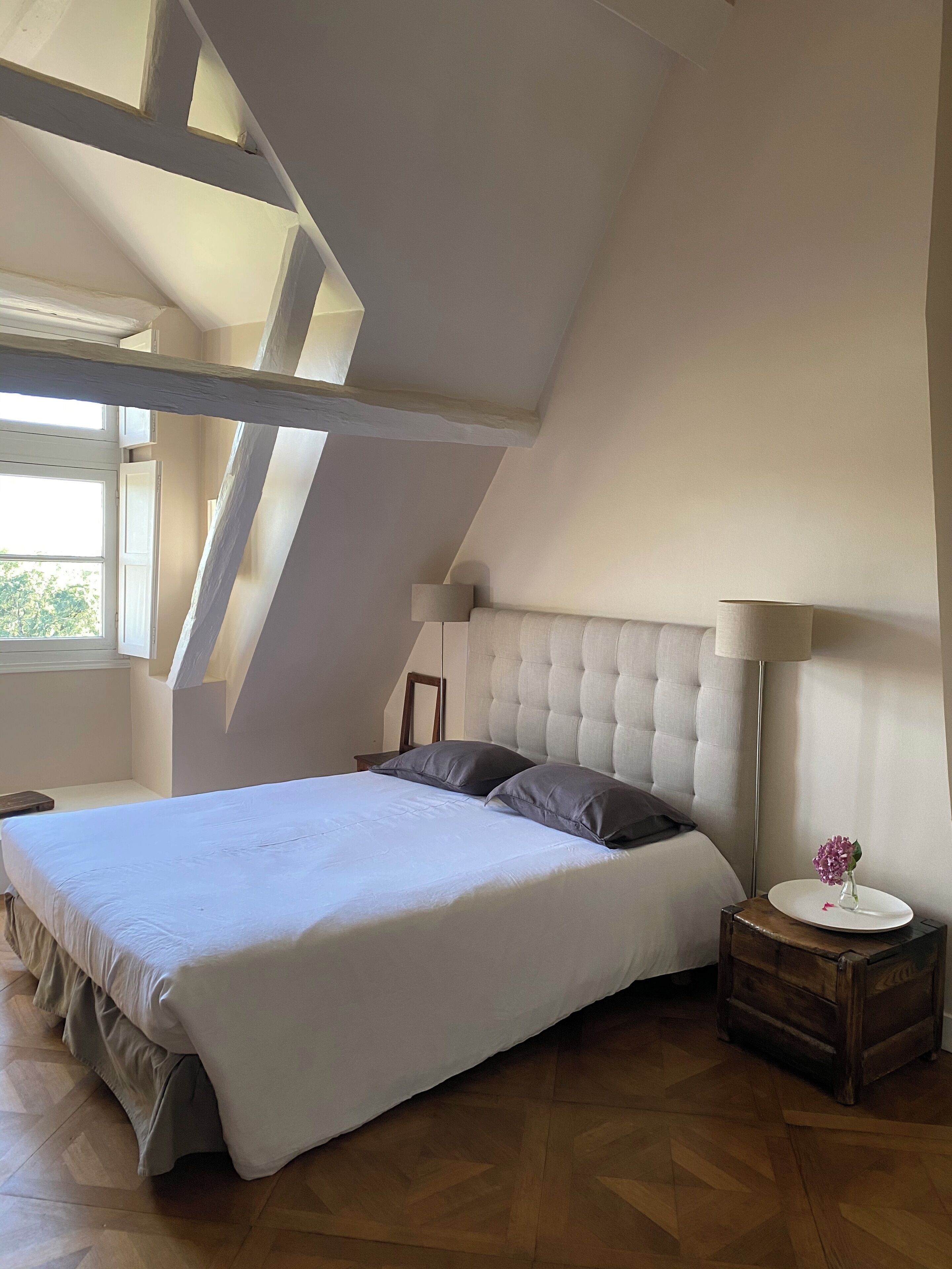 A bedroom with a large bed, a nightstand, a lamp, and a window.