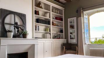 A bedroom with a fireplace, built-in shelving, a bed, and a view through a window.