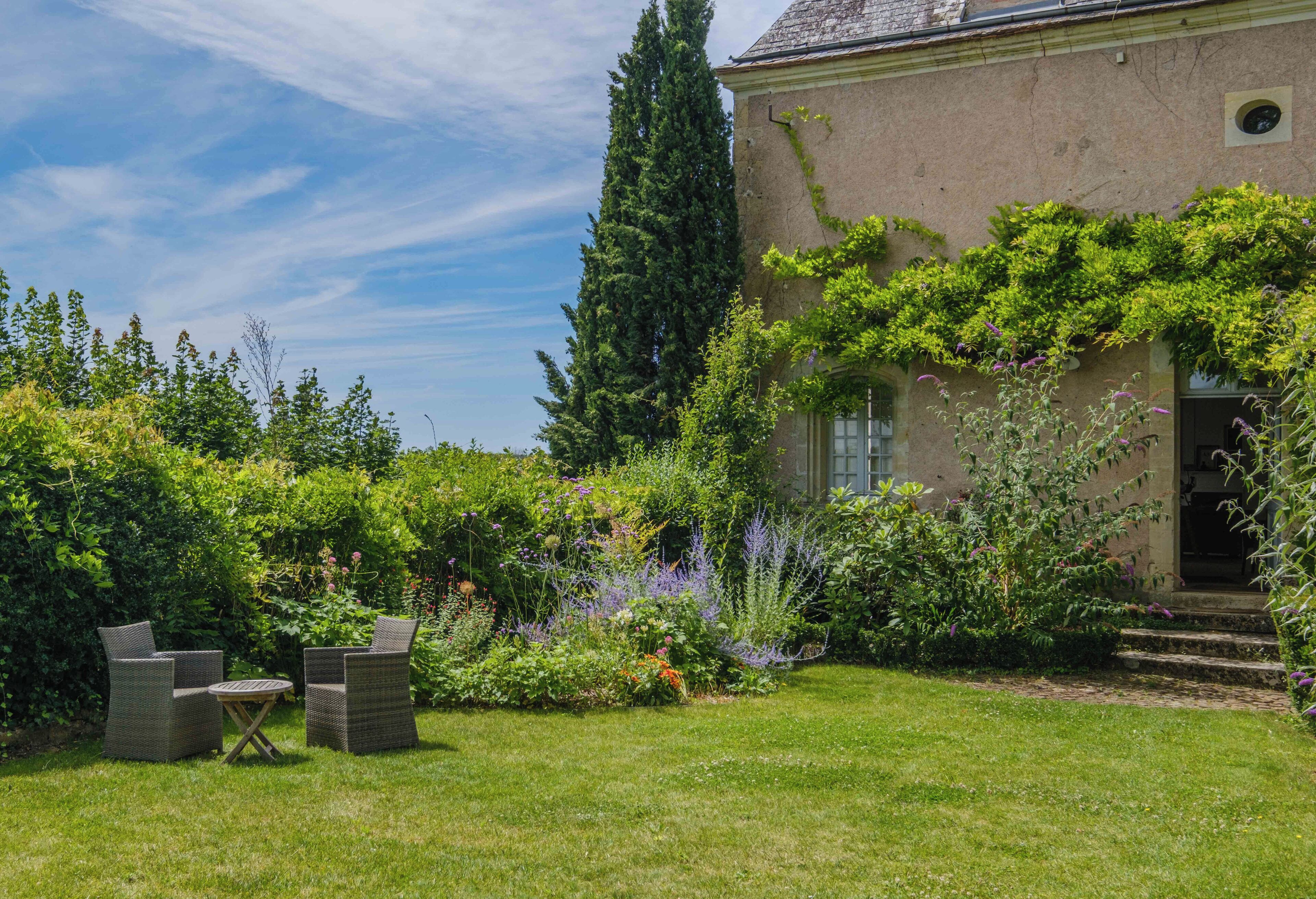 Un jardin avec un bâtiment, deux chaises en osier et une petite table.
