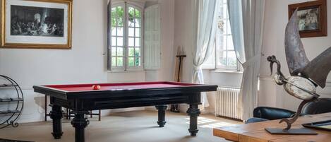 A room with a pool table, a billiards rack, a framed picture, a window with curtains, and a statue.