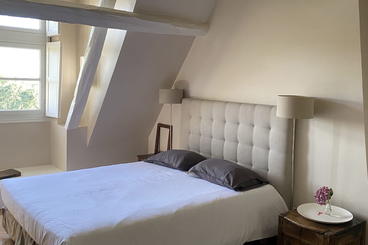 Une chambre à coucher avec un grand lit, une table de chevet, une lampe et une fenêtre.