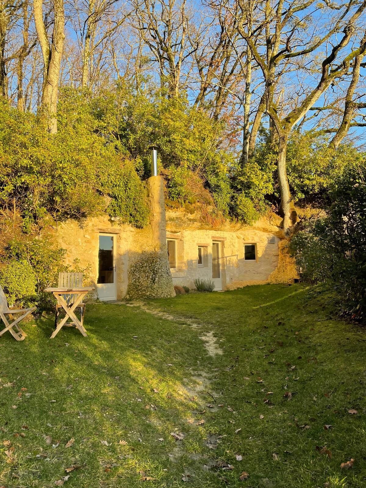 A rustic stone building with a chimney, surrounded by trees and a grassy yard.