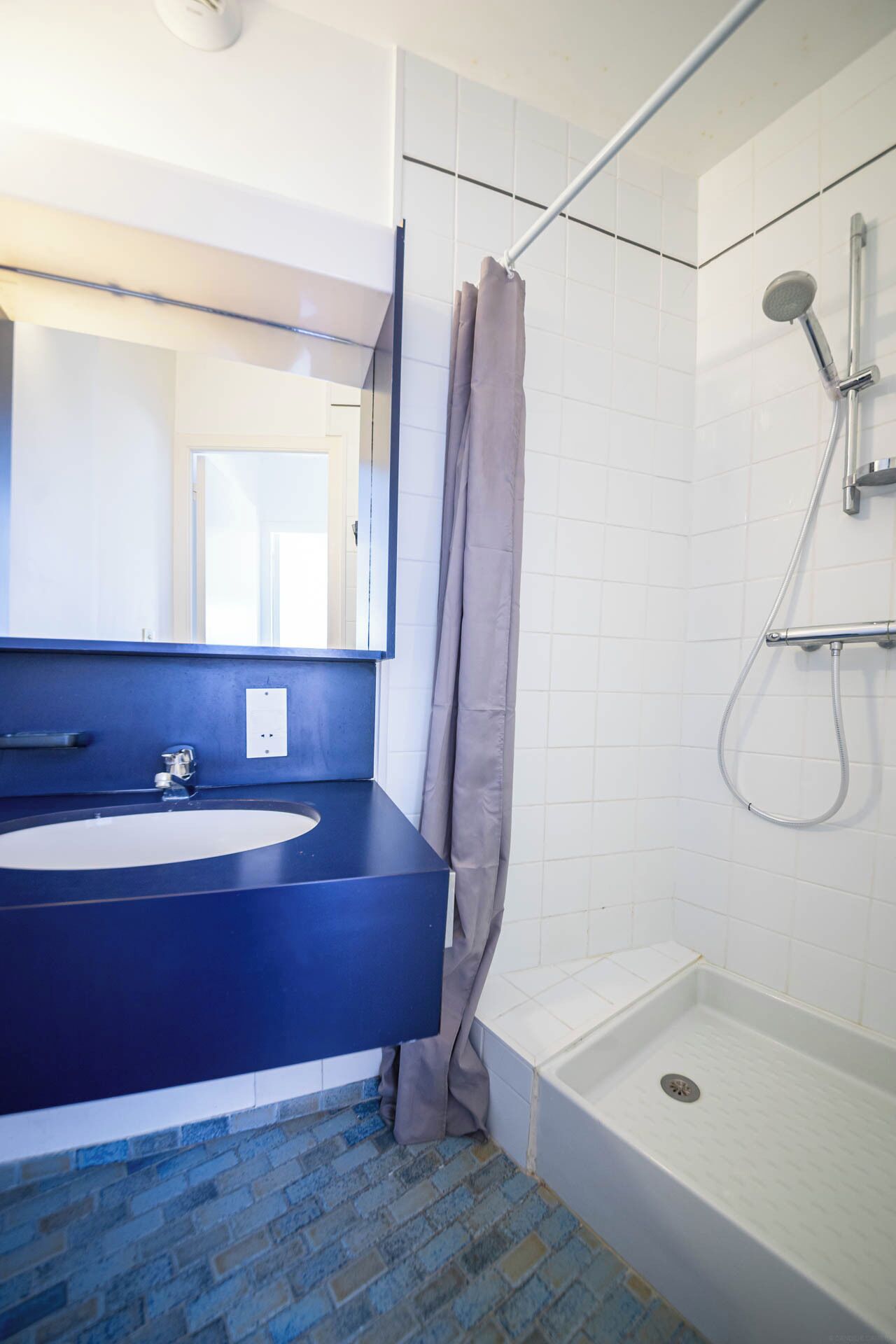 A bathroom with a blue sink, a shower, and a mirror.